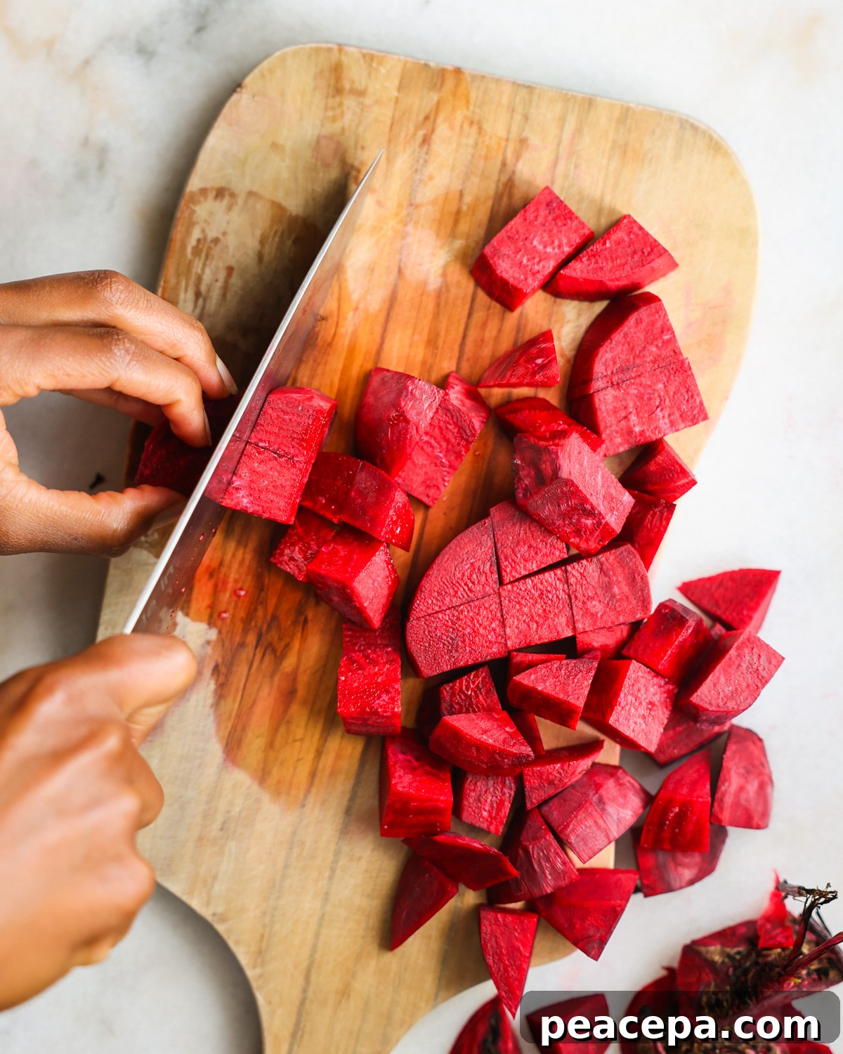 An overhead shot of brown hands slicing beets into chunks.