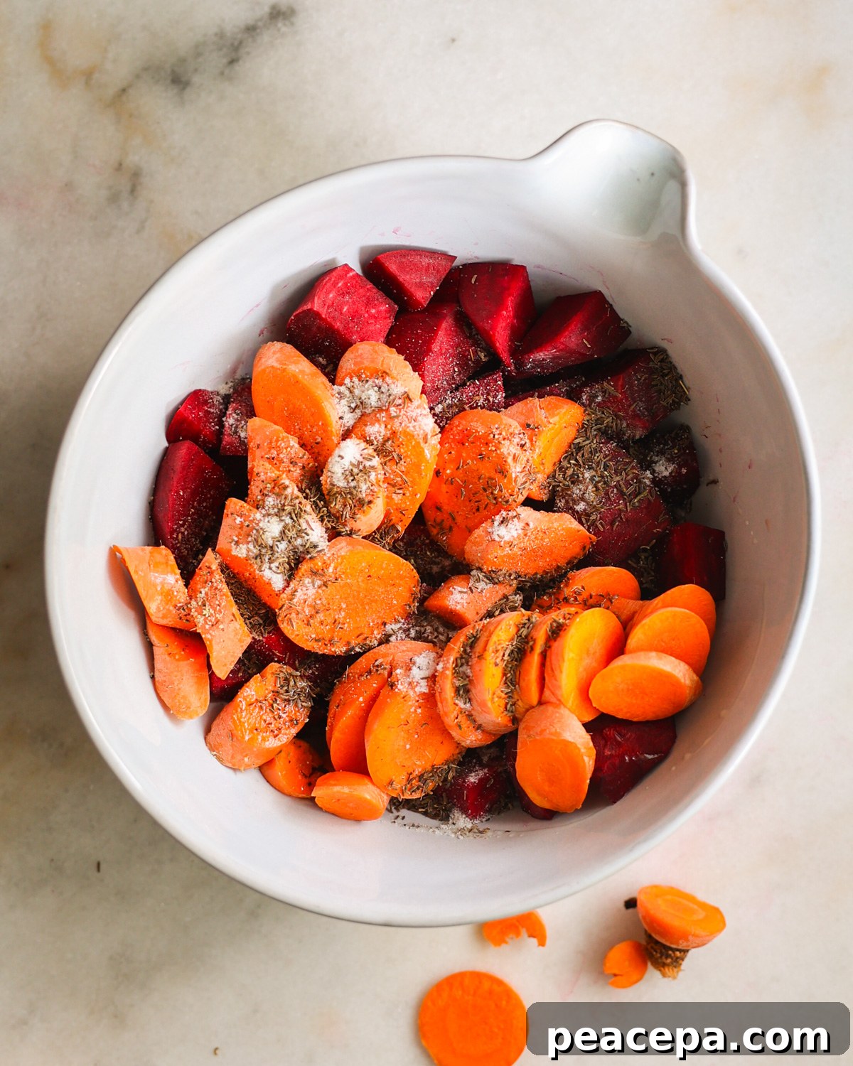 The beets and carrots in a mixing bowl with oil and seasoning before mixing.
