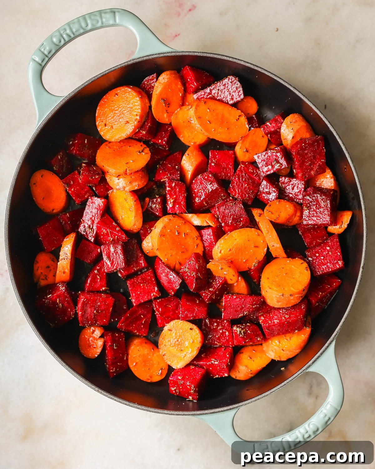 An overhead shot of the seasoned beets and carrots before roasting.