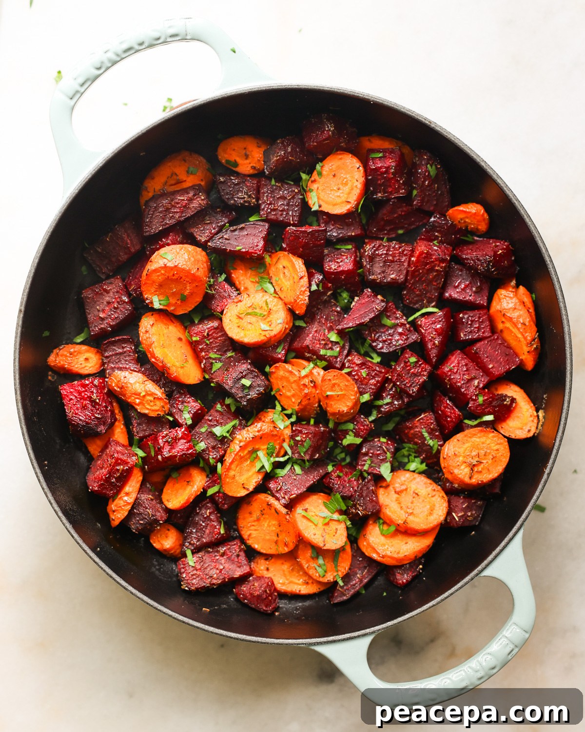An overhead shot of a white pan of roasted beets and carrots with herbs.