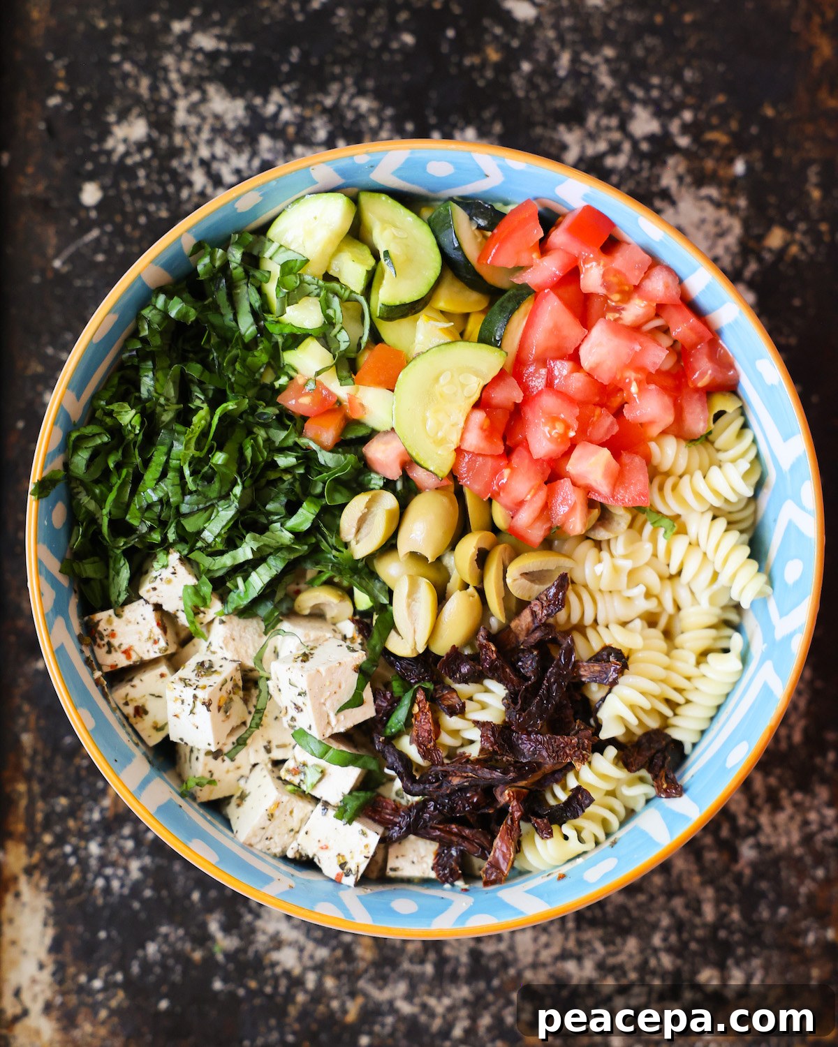 An overhead shot of a patterned blue bowl with pasta, veggies, and marinated tofu.