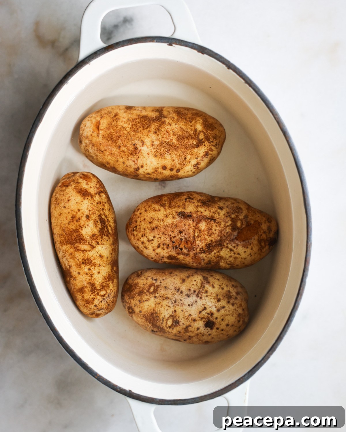 overhead of whole russet potatoes in a pot of water