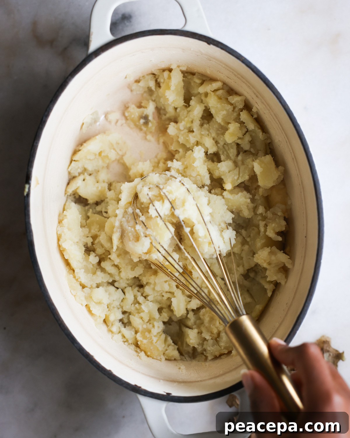 overhead of a hand using a whisk to mash potatoes