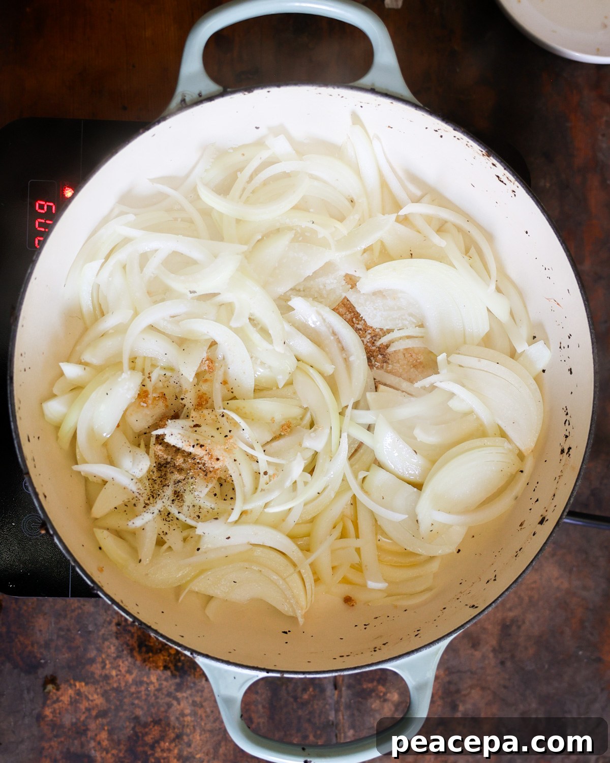 An overhead shot of the sliced onions with salt, pepper, and brown sugar in a pan.
