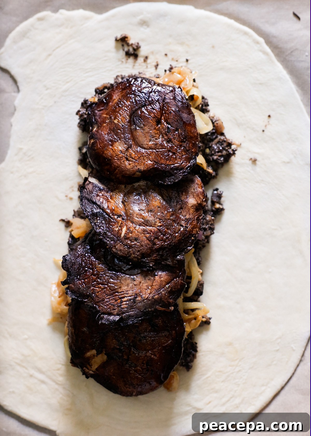 An overhead shot of puff pastry topped with the mushroom filling, caramelized onions, and portobello mushrooms layered on each other.