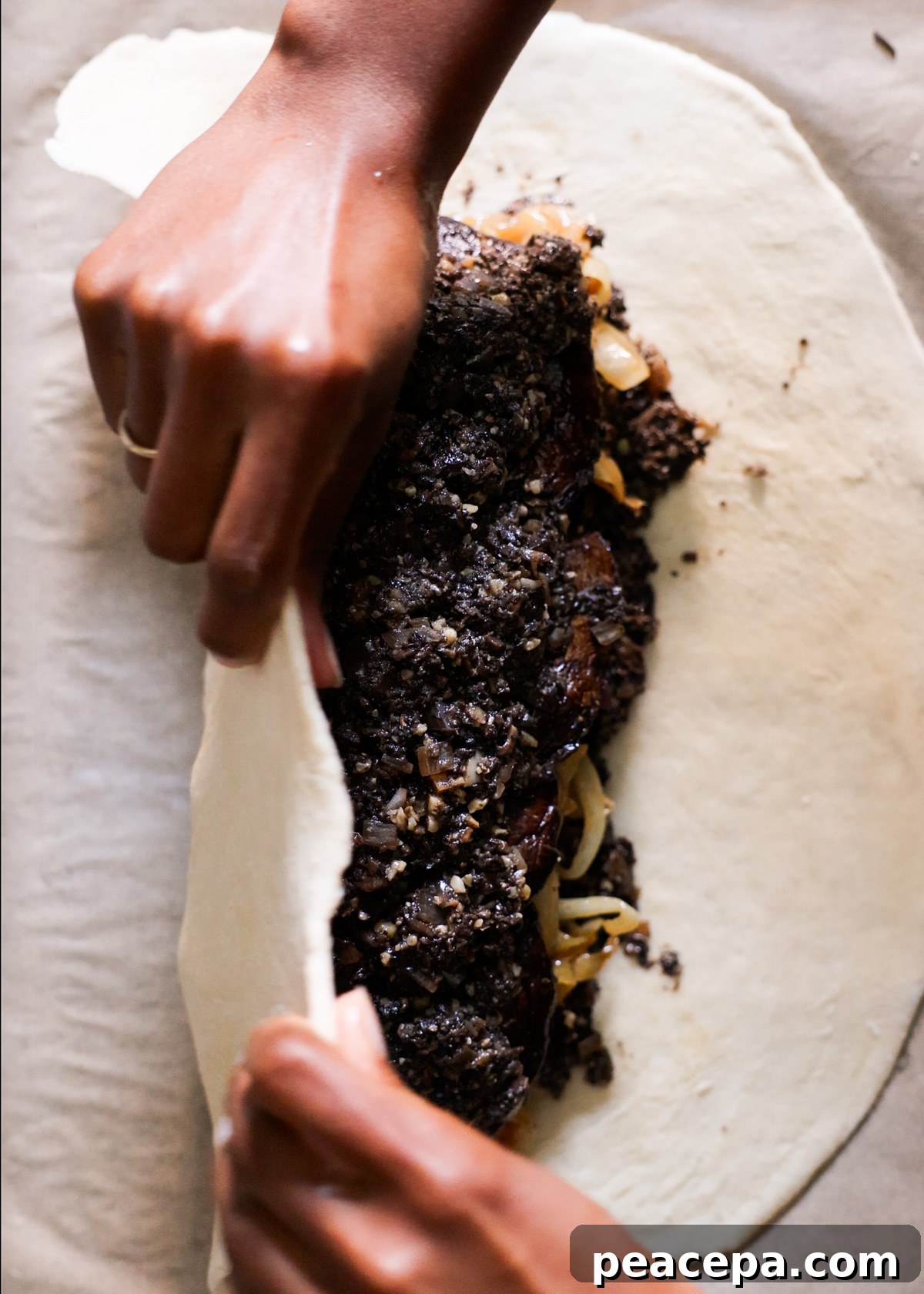 Two brown hands turning the pastry over the vegetable filling.