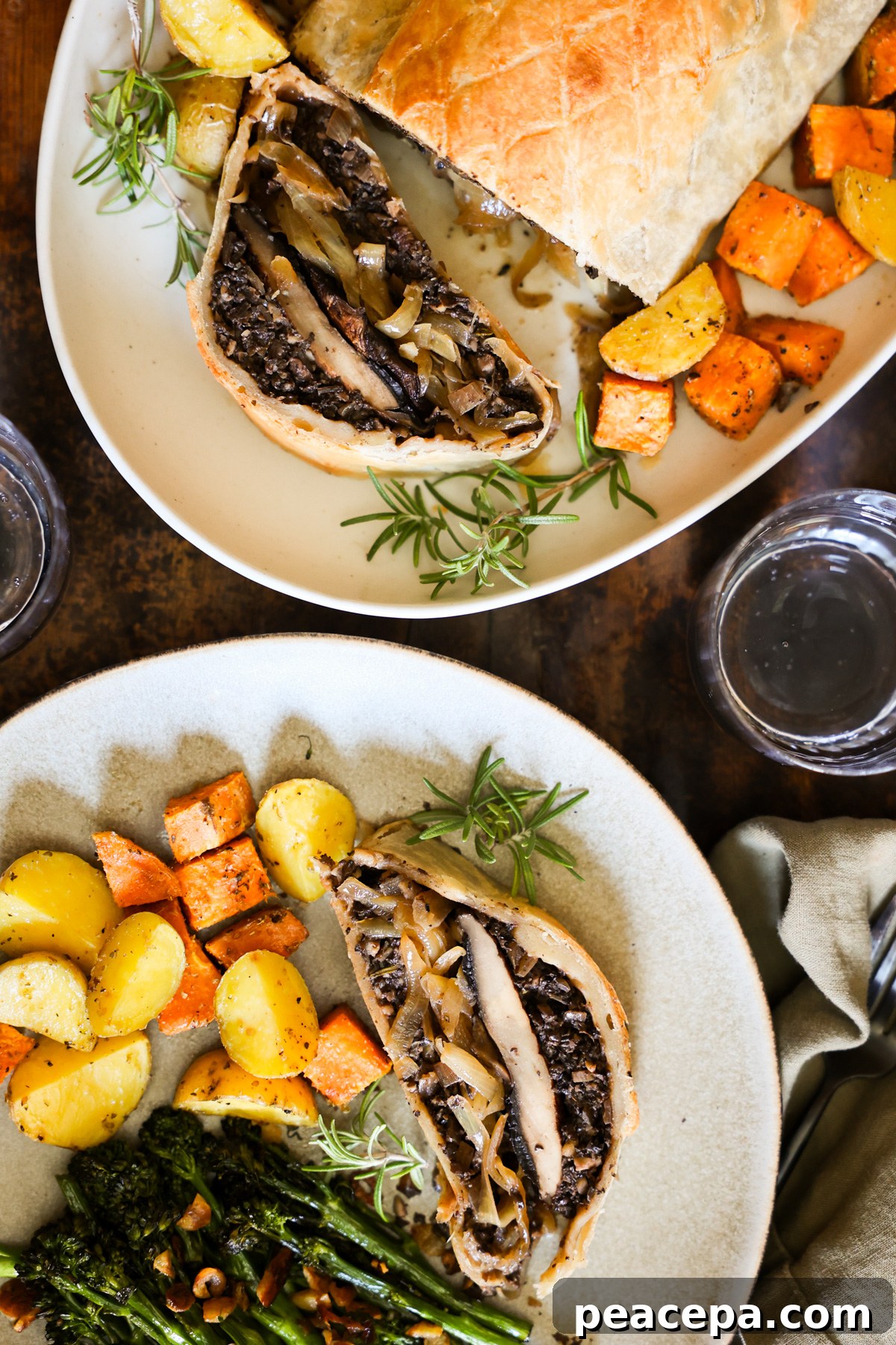 An overhead shot of a dinner plate with roasted vegetables and a piece of mushroom Wellington next to a serving plate of it.
