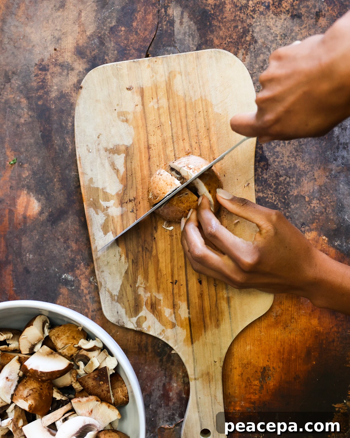 An overhead shot of two brown hands roughly chopping mushrooms.