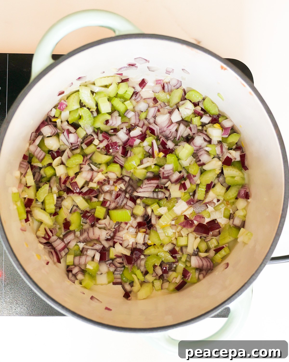 An overhead shot of red onions and celery cooking in a large pot.