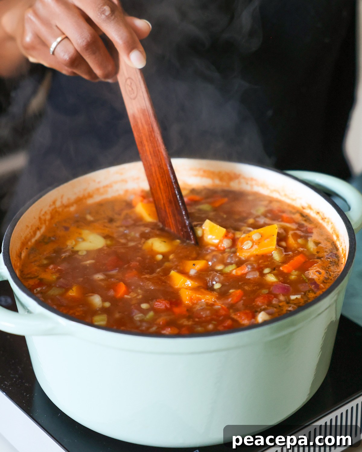 A brown hand stirring a pot of the butternut squash and lentil soup as it cooks.