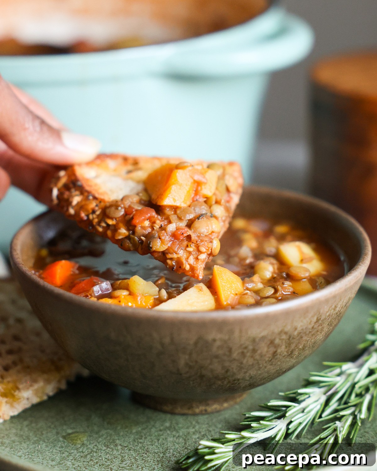 A close-up shot of a hand tipping a piece of toasted sourdough bread in the butternut squash lentil soup.