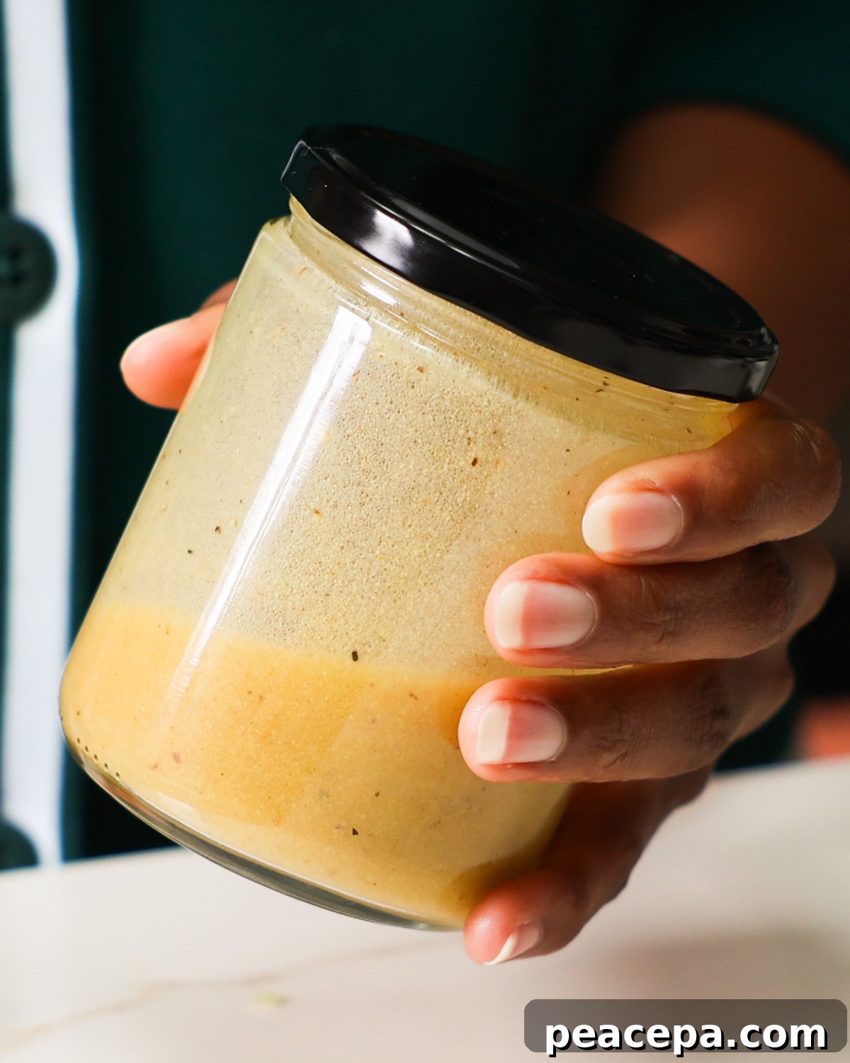 A brown hand mixing the black bean and corn salad dressing in a lidded jar.