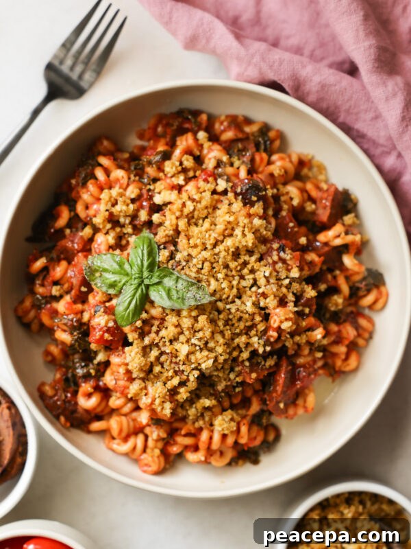 An overhead shot of a white bowl of Instant Pot Vegan Sausage Pasta with bread crumbs and a sprig of basil.