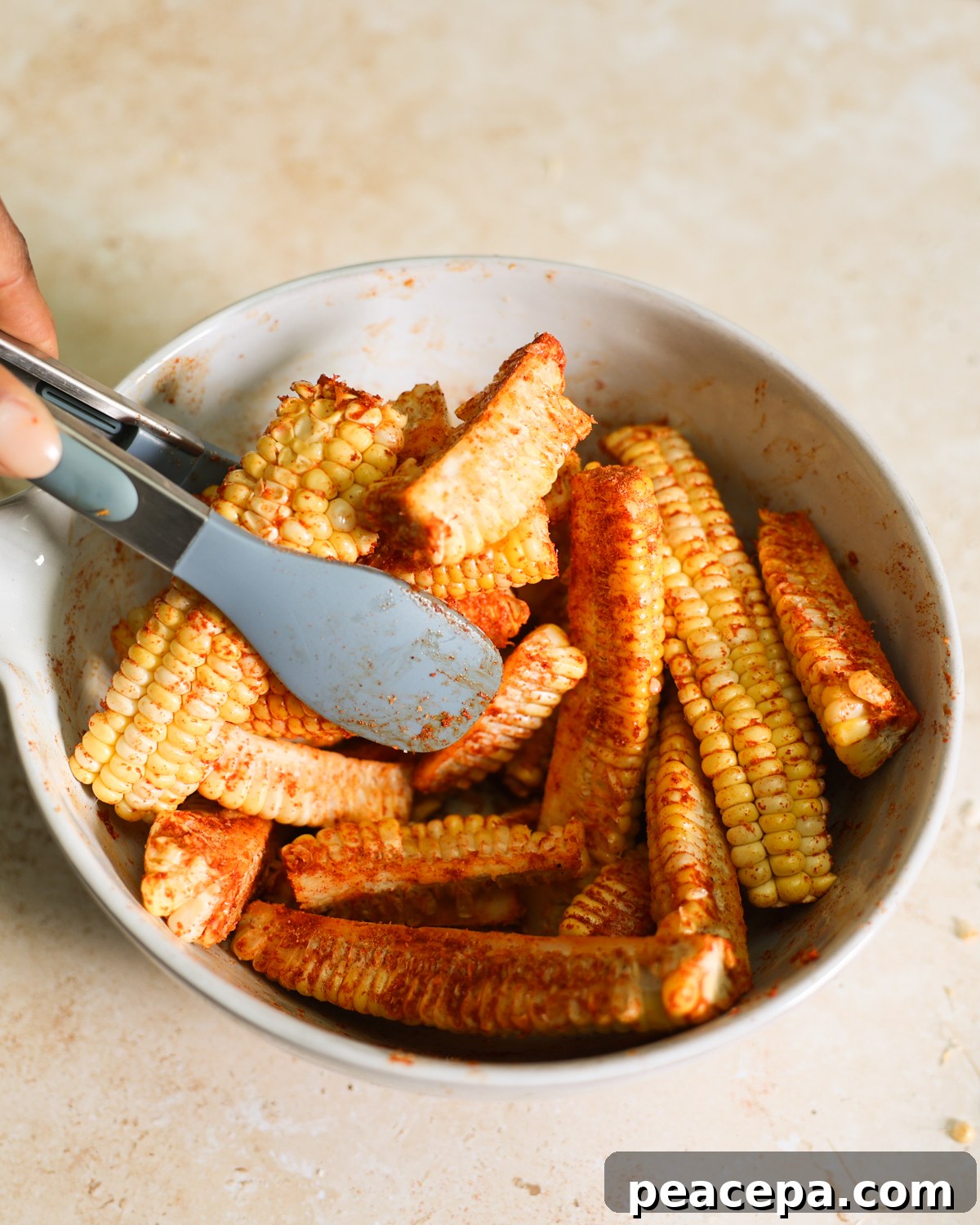 tongs tossing corn in spices