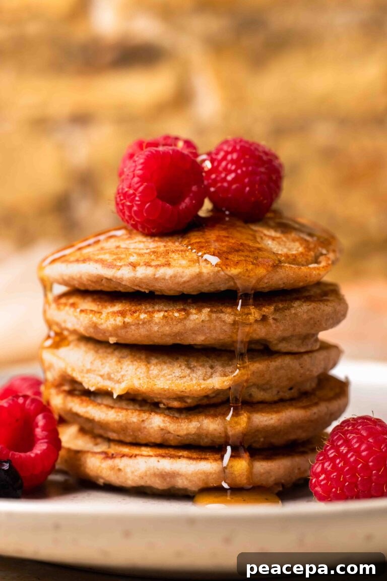 An up-close side shot of a small stack of spelt pancakes with raspberries and maple syrup.