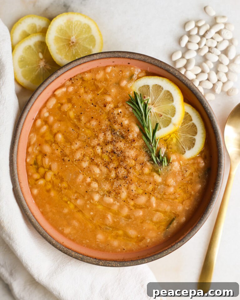 A bowl of Instant Pot white beans with lemon and rosemary garnish.