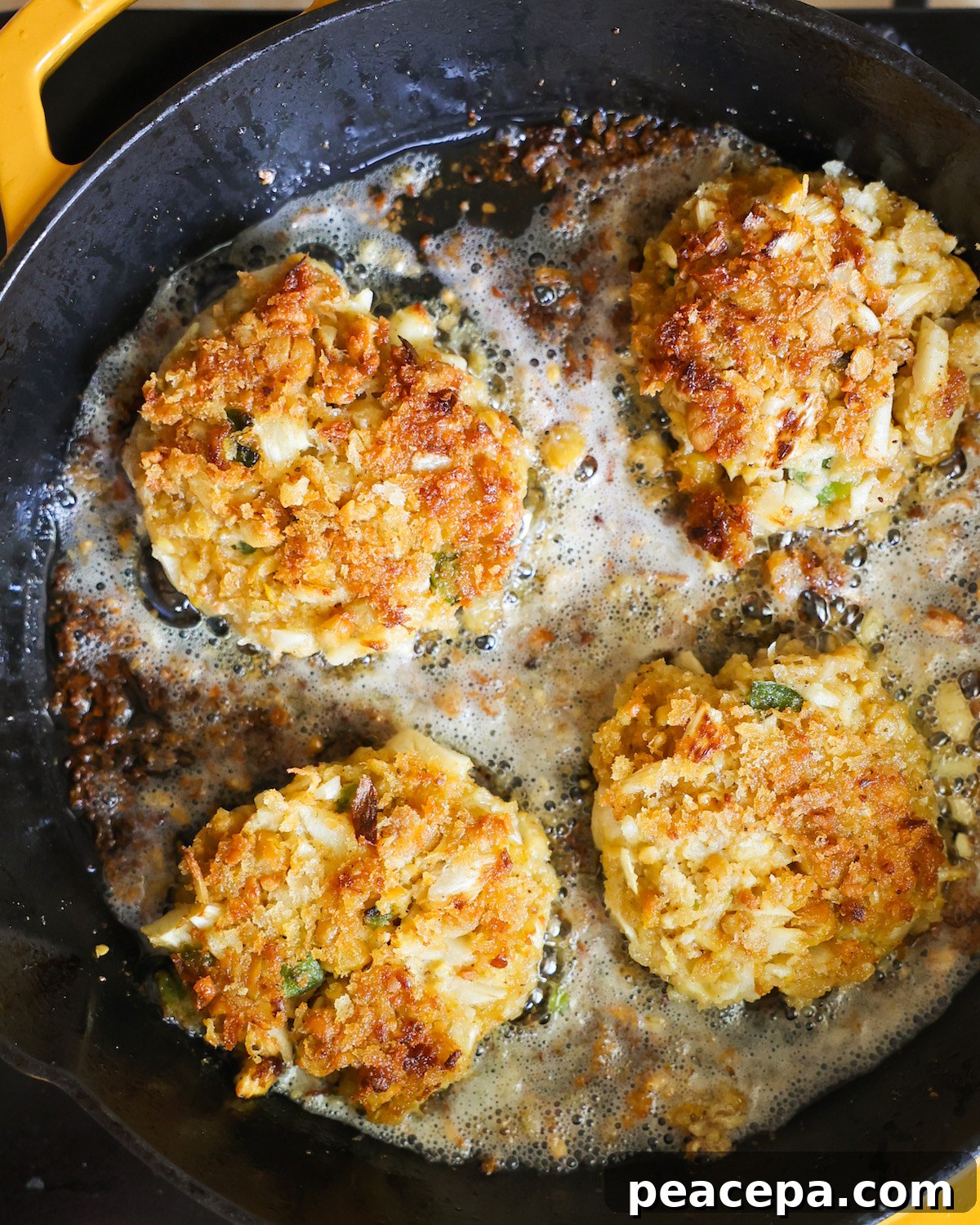 overhead of four vegan crab cakes frying in a cast iron skillet