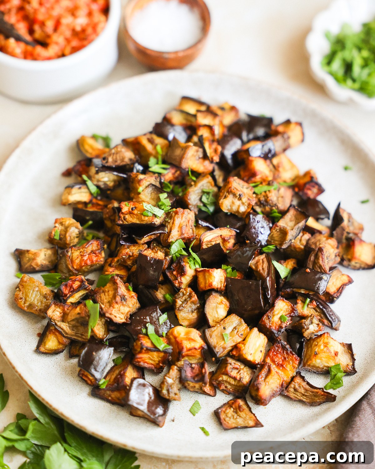A close-up angled shot of a small serving plate of air fryer eggplant topped with chopped herbs.