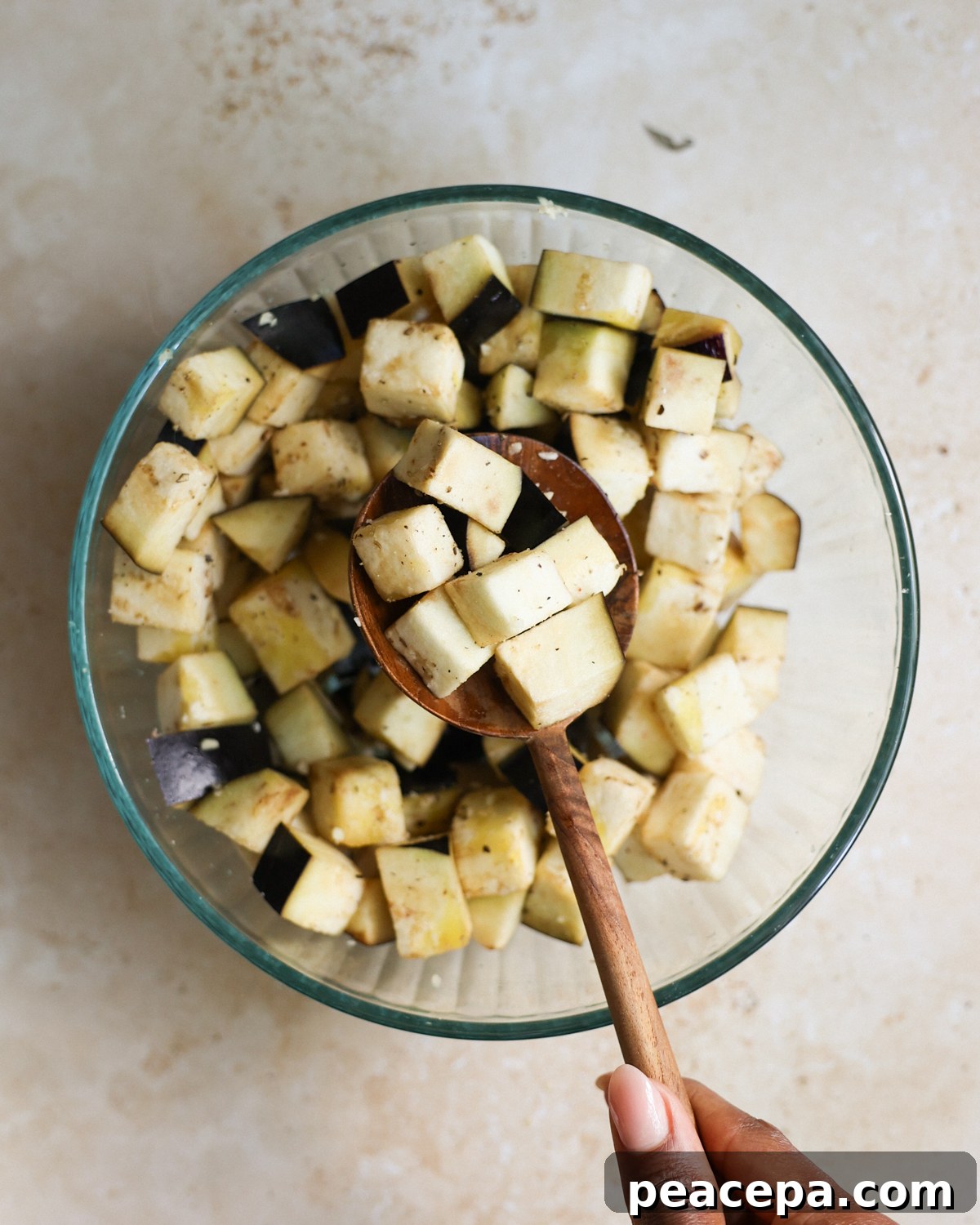 A brown hand holding a stirring spoon with seasoned eggplant on it.
