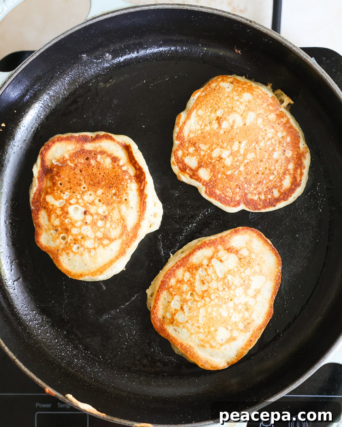 An overhead shot of three sourdough discard pancakes cooking on the griddle.
