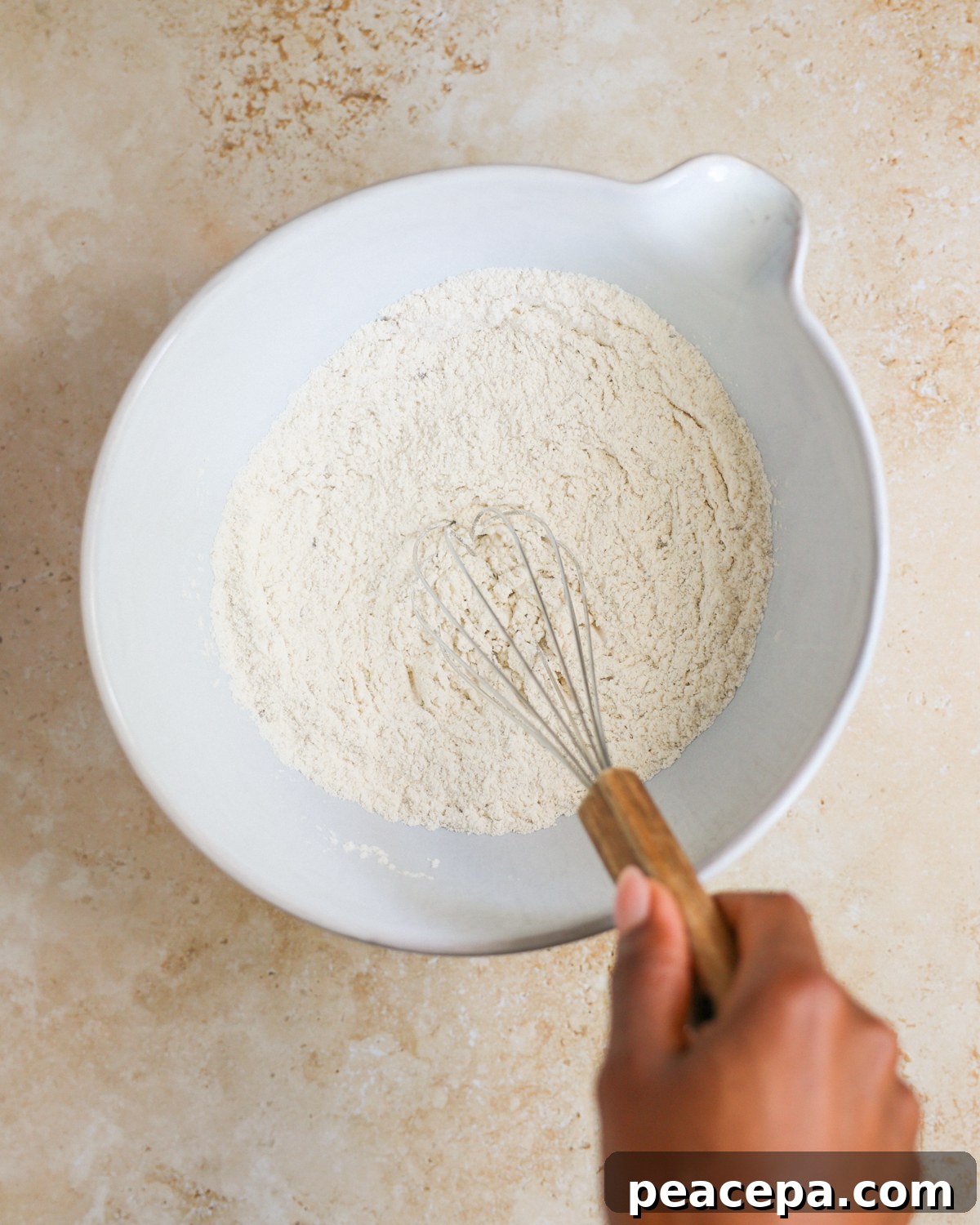 A brown hand whisking the bowl of dry ingredients.