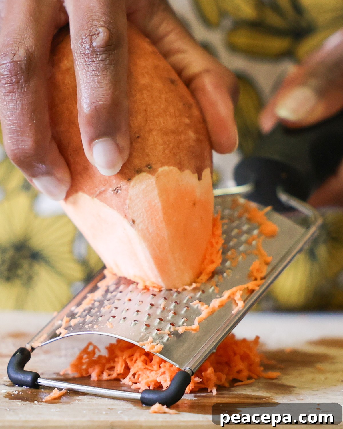 An up-close shot of a brown hand shredding a sweet potato on a cutting board.