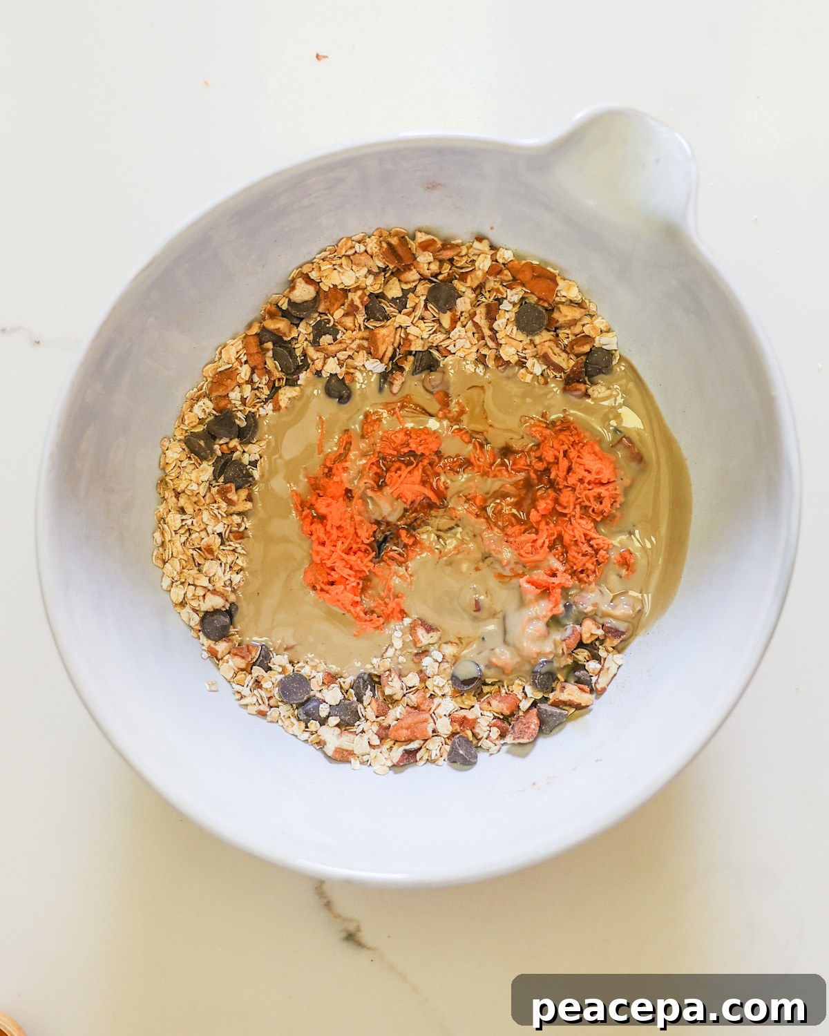 A mixing bowl of the oats, pecans, chocolate chips, tahini, and shredded sweet potatoes.
