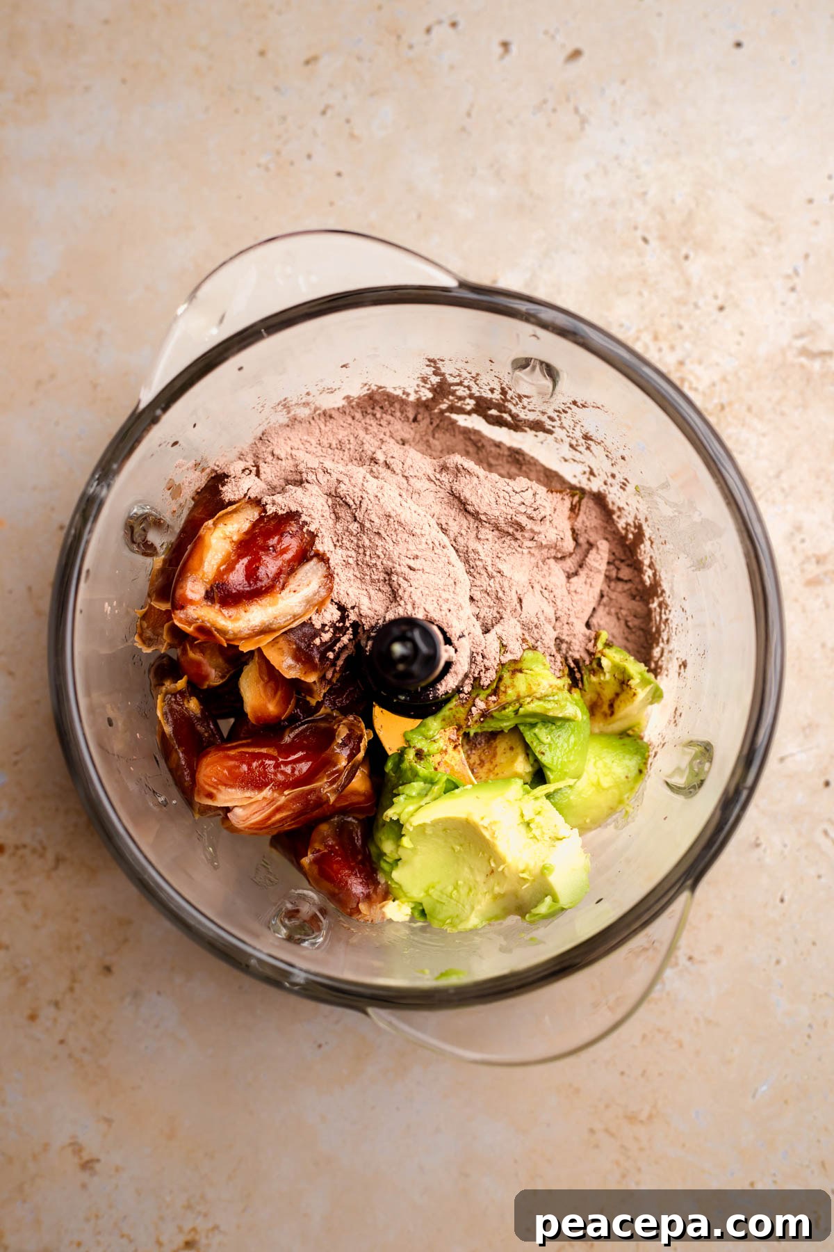 The avocado, dates, and cacao powder in the bowl of a food proccesor.