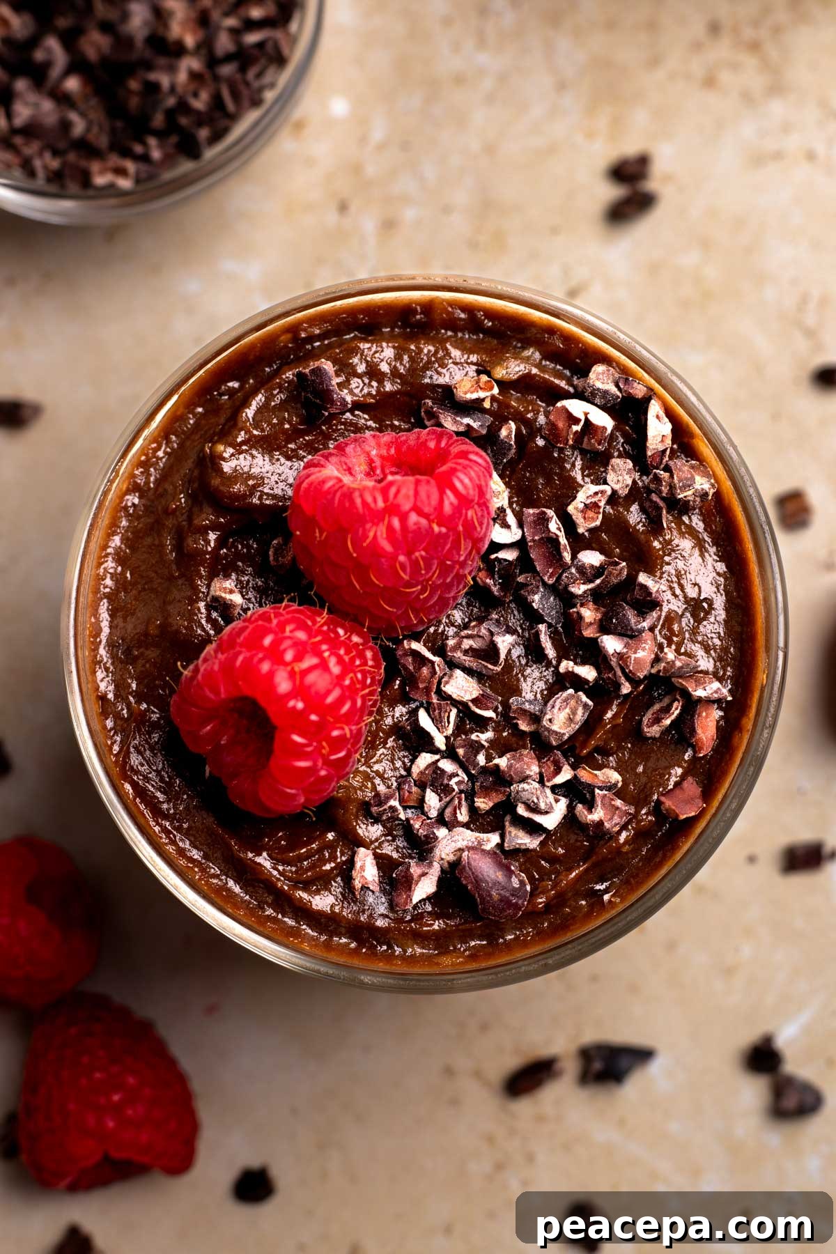 An overhead shot of a small dish of vegan chocolate mousse topped with carob chips and raspberries.