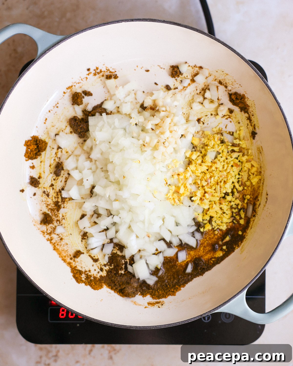 A white pan of toasted curry paste with onions, garlic, and ginger added.