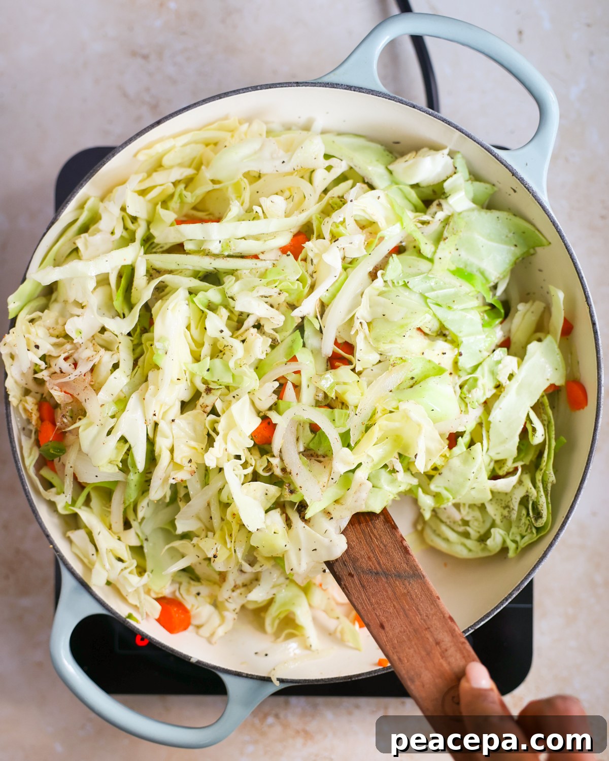Stirring jamaican braised cabbage in skillet. 