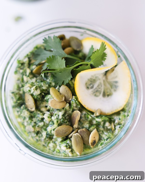 Glass bowl of Pepita Cilantro Pesto topped with fresh herbs and a lemon slice.