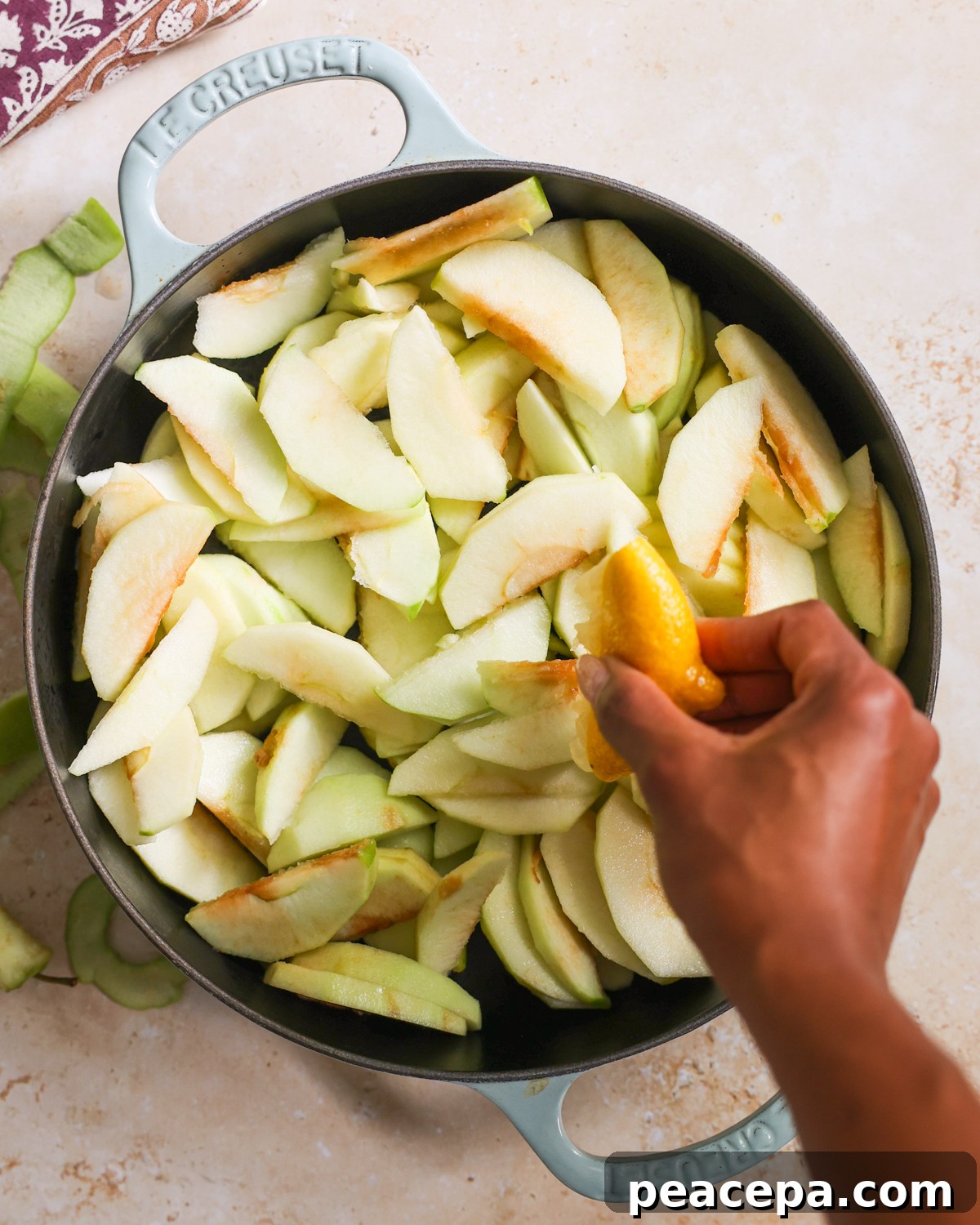 Hand squeezing lemon over apples in a cast iron skillet.