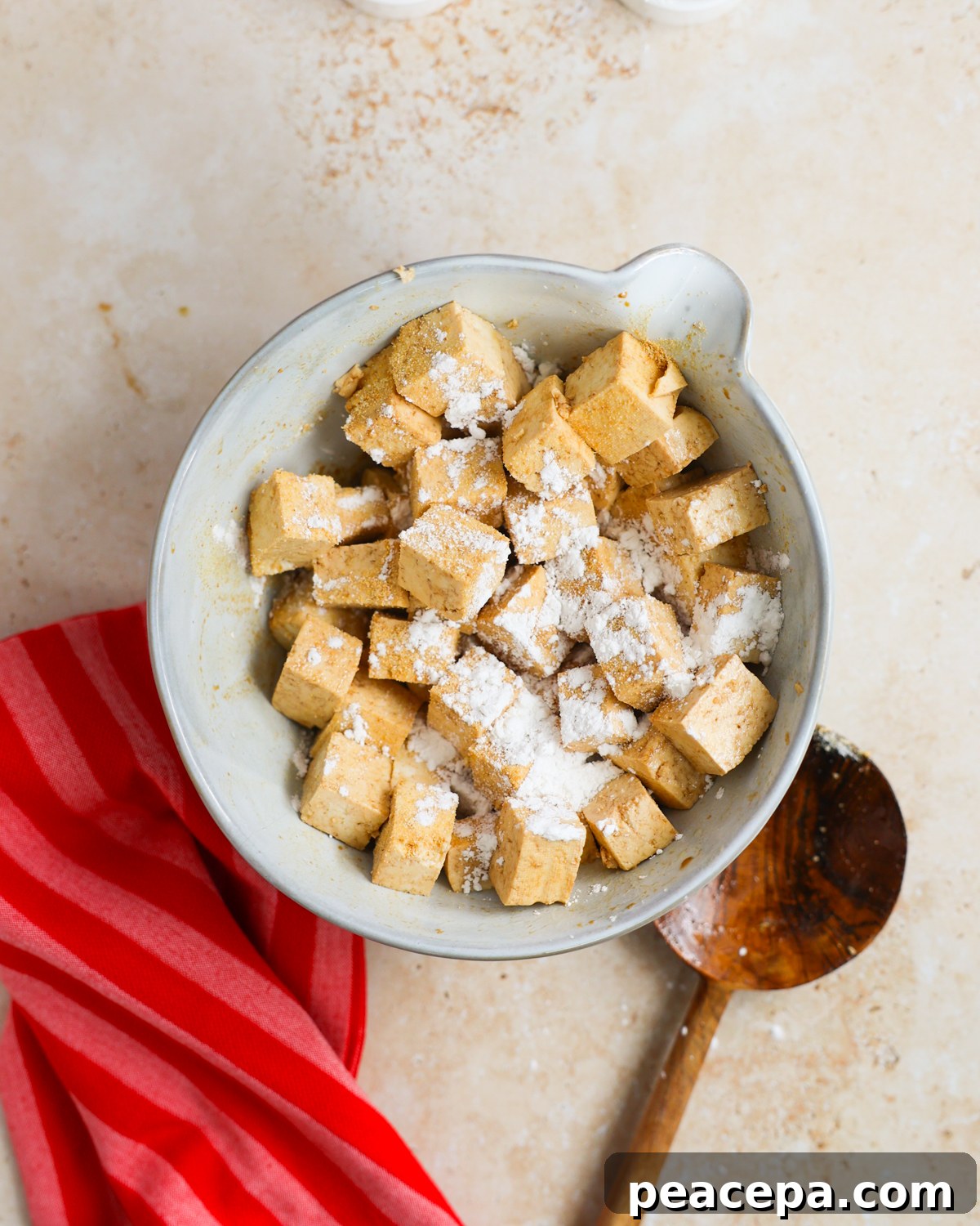 Tofu topped with cornstarch in mixing bowl.