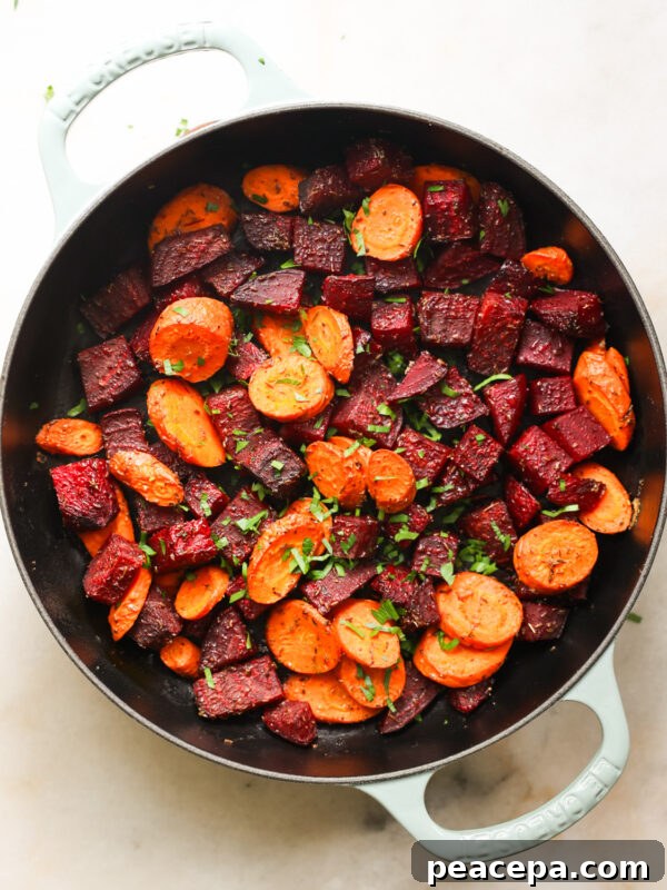 An overhead shot of a white pan of roasted beets and carrots with herbs.