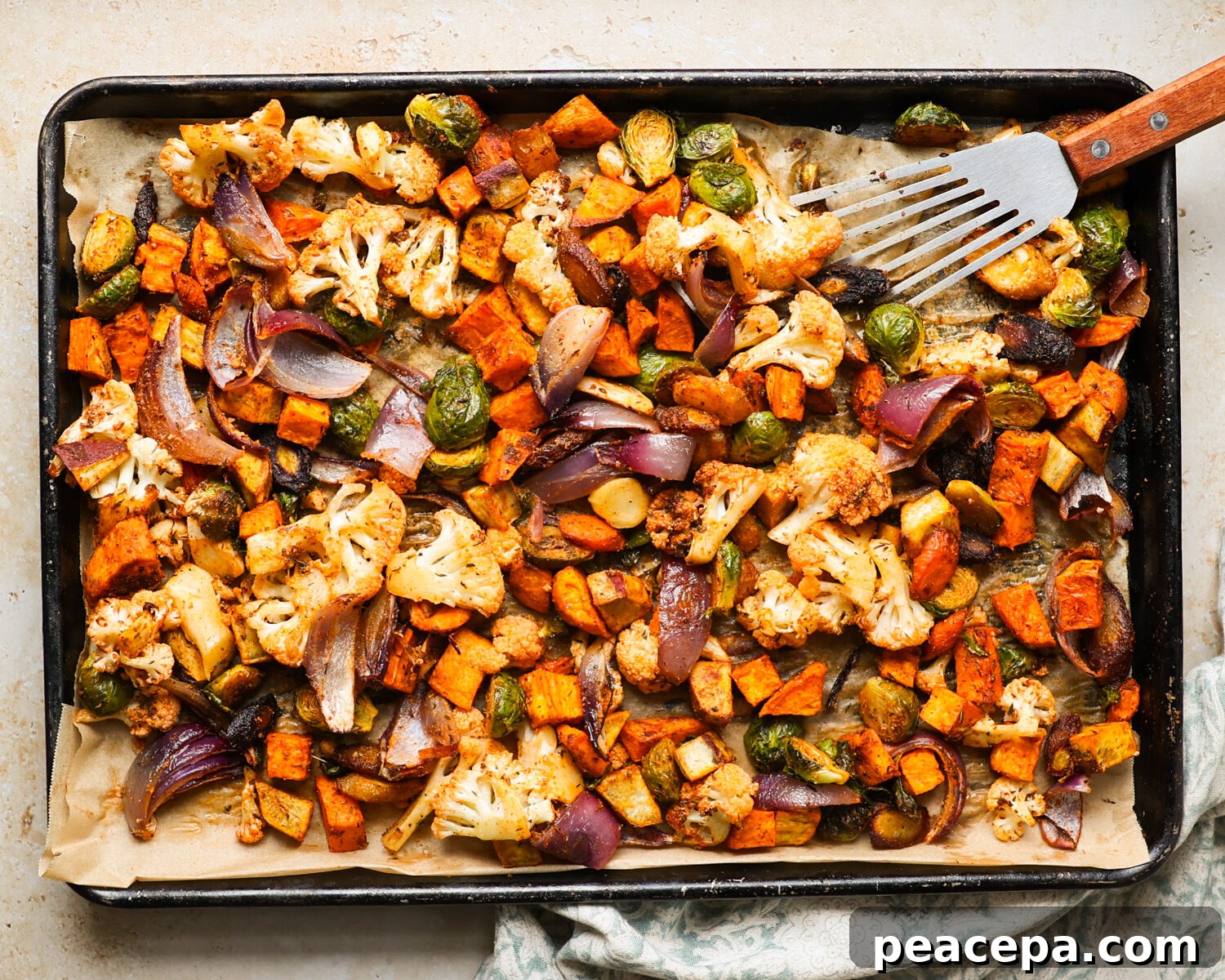 Stirring roasted vegetables on a baking tray.