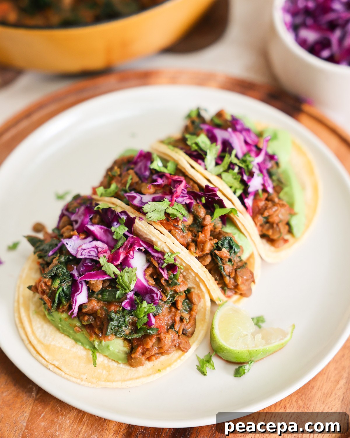 Colorful lentil tacos on a white plate in front of a yellow skillet. 