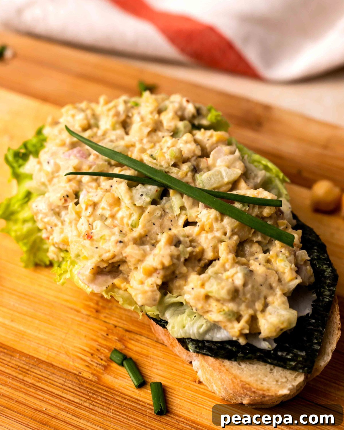 A closeup shot of vegan chickpea salad on toast on a wooden cutting board.