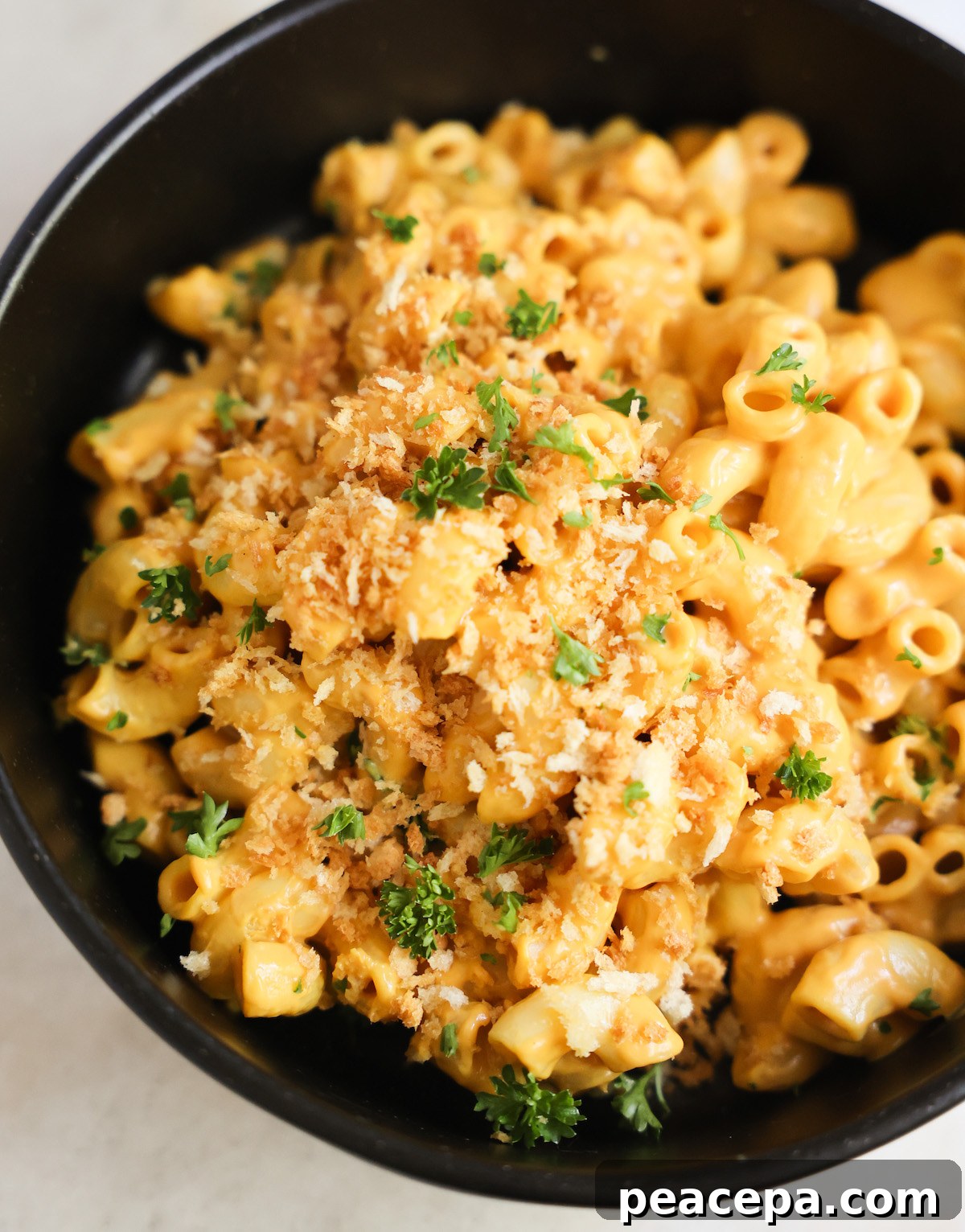 A close-up shot of vegan butternut squash mac and cheese in a black bowl with panko breadcrumbs.