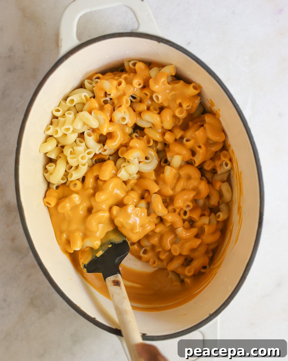 An overhead shot of stirring the macaroni in with the butternut squash mac and cheese sauce.