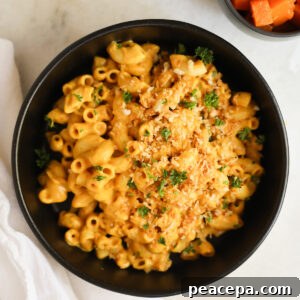 An overhead shot of a black bowl of vegan butternut squash mac and cheese topped with breadcrumbs and minced parsley.