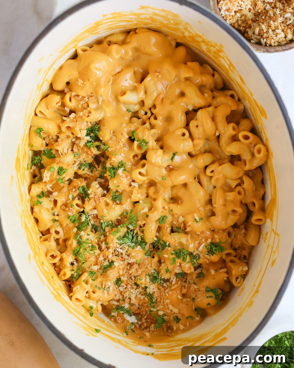 An overhead shot of a white pan of vegan butternut squash mac and cheese with panko breadcrumbs and minced parsley.