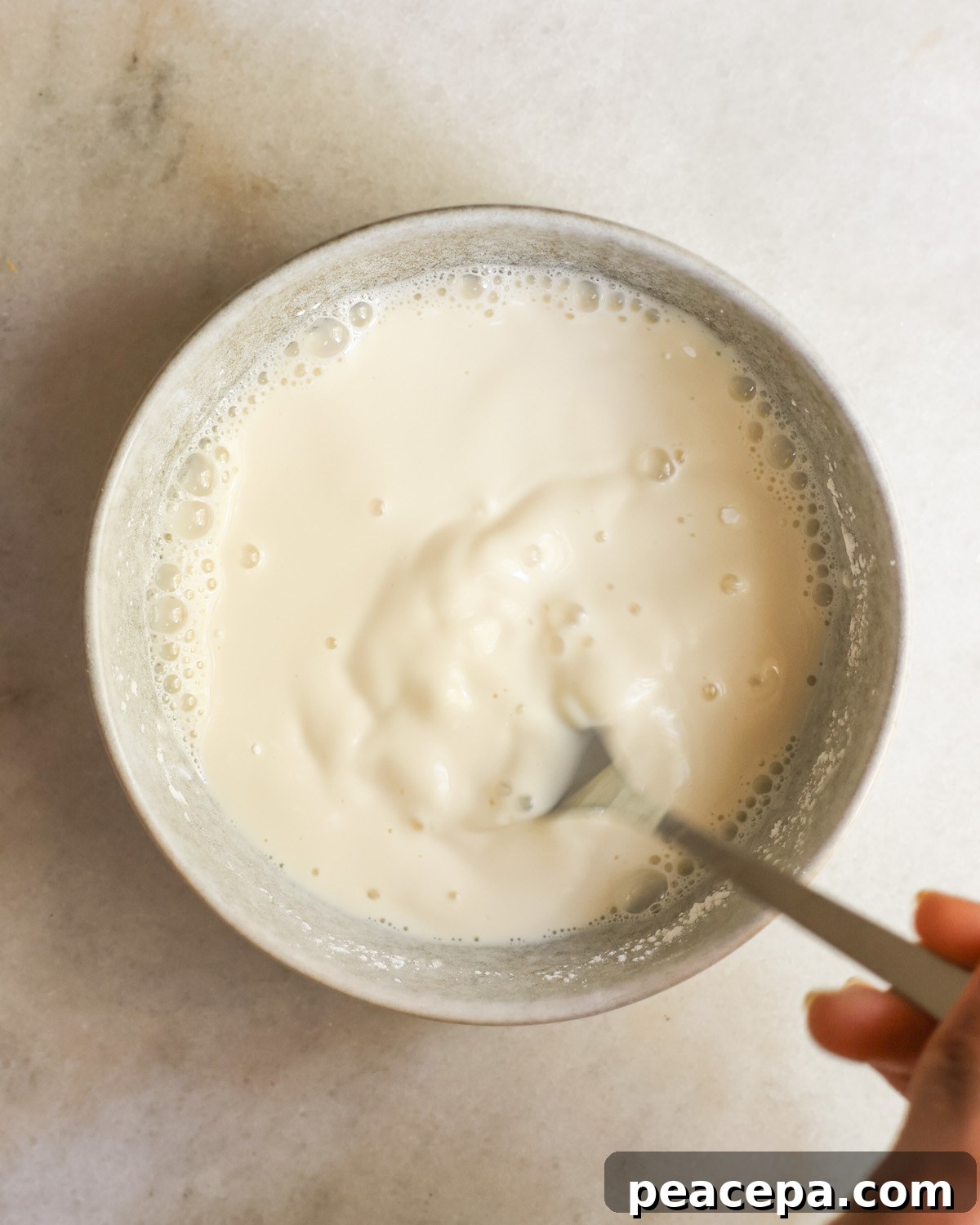 Whisking the arrowroot powder and milk in a grey bowl.