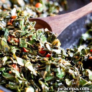 Wooden spoon scooping collard greens in a skillet.