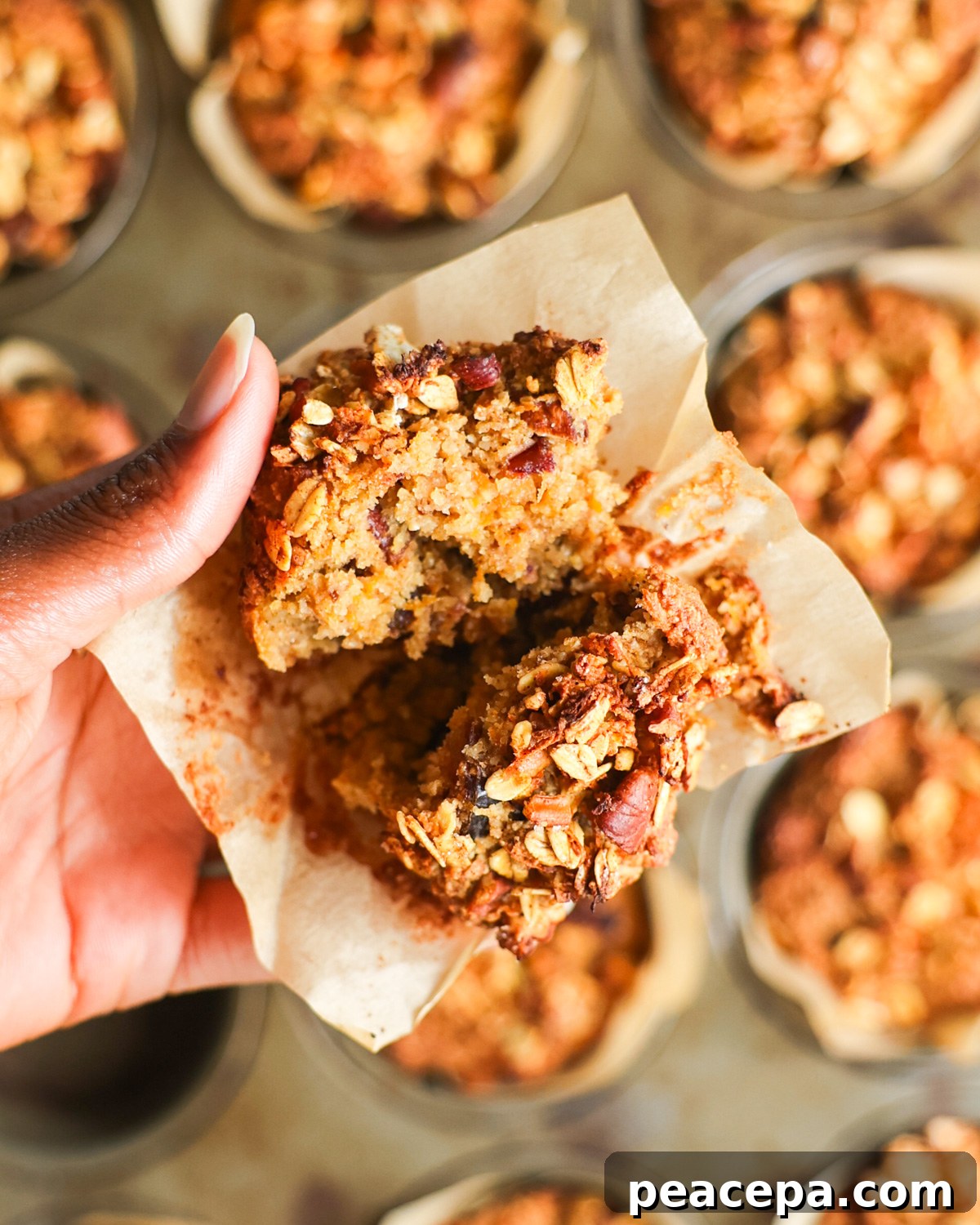 A close-up overhead shot of a brown hand holding an oat bran muffin split in half.