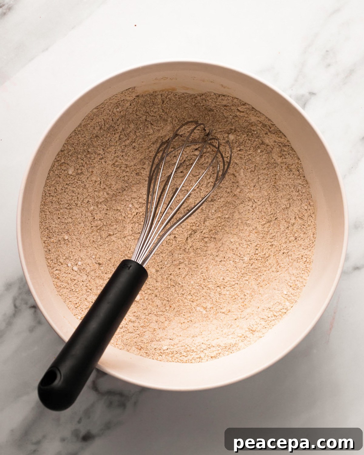 An overhead shot of a bowl of whisked whole wheat flour with a whisk.
