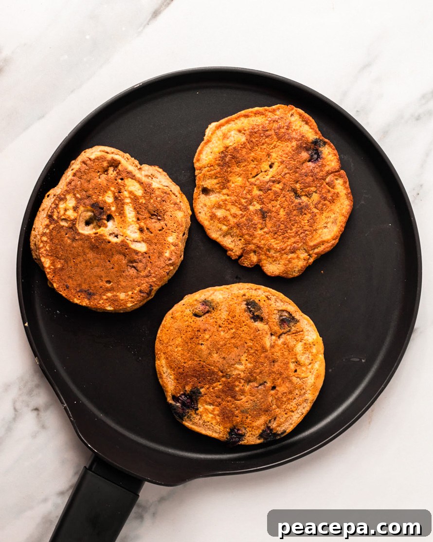 A skillet with three vegan blueberry pancakes on top.