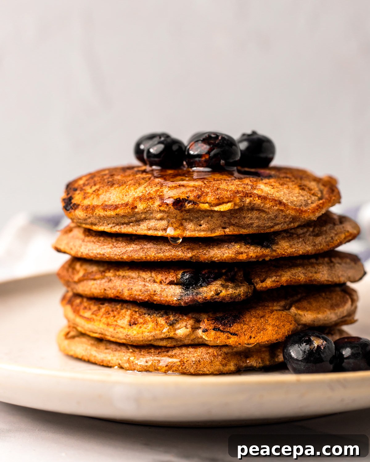 A side shot of a stack of vegan blueberry pancakes with a bit of maple syrup on top.