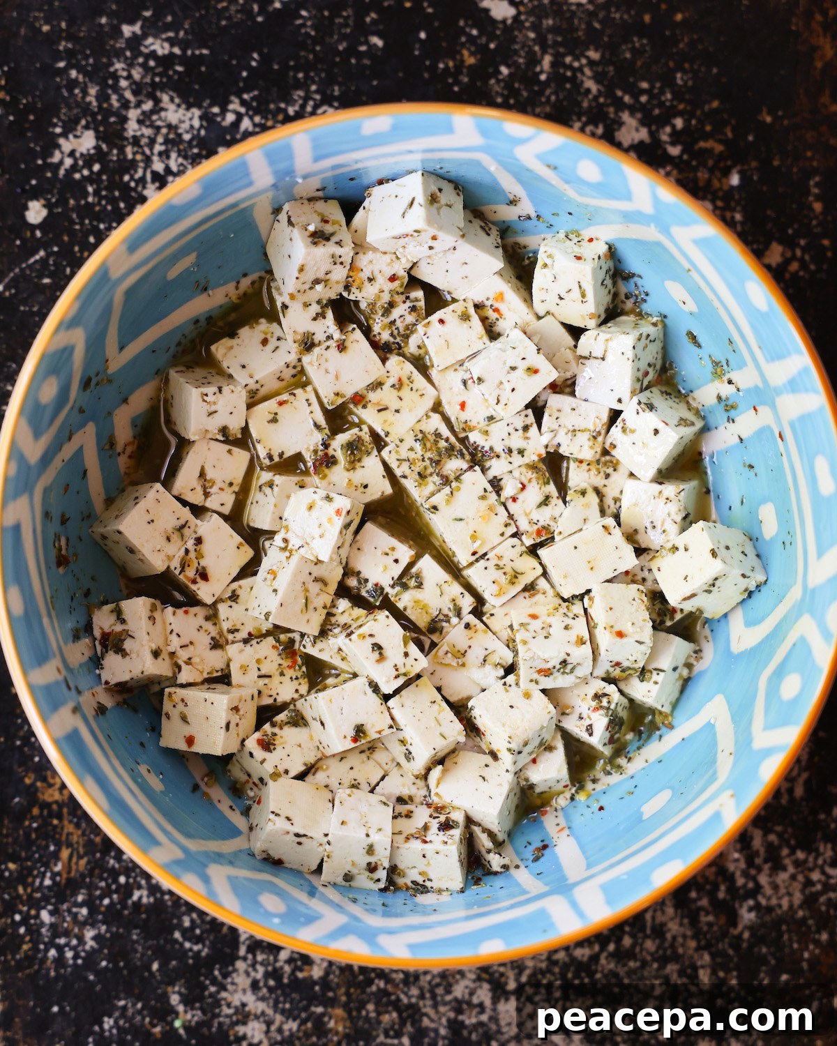 An overhead shot of a blue patterned bowl of marinating tofu cubes.