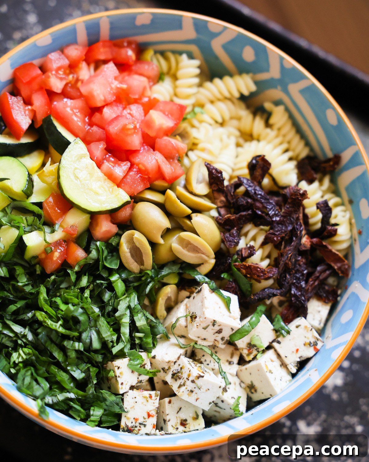 An up-close side shot of a blue patterned bowl of Mediterranean pasta salad.